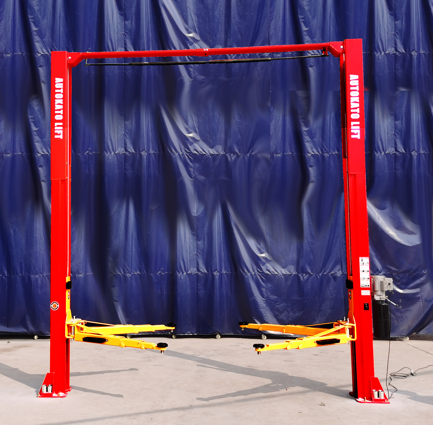 Red automotive lift with yellow parts against a blue tarp background